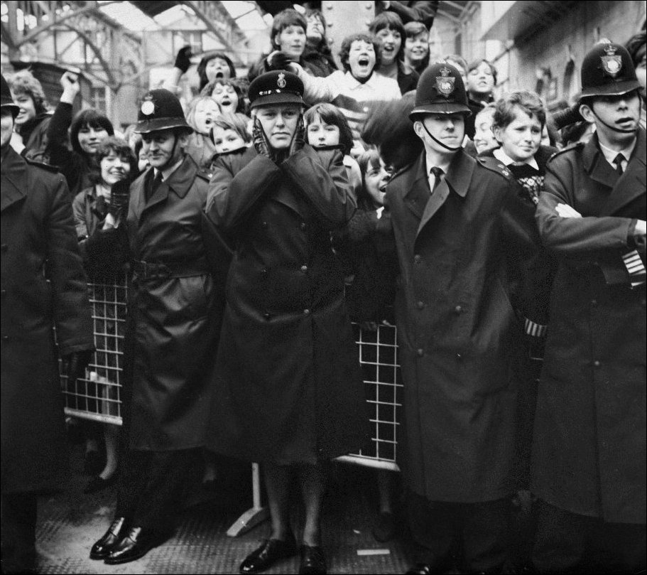 6 апреля 1964. Лондон. Женщина-полицейский закрывает уши в окружении кричащих фанатов группы