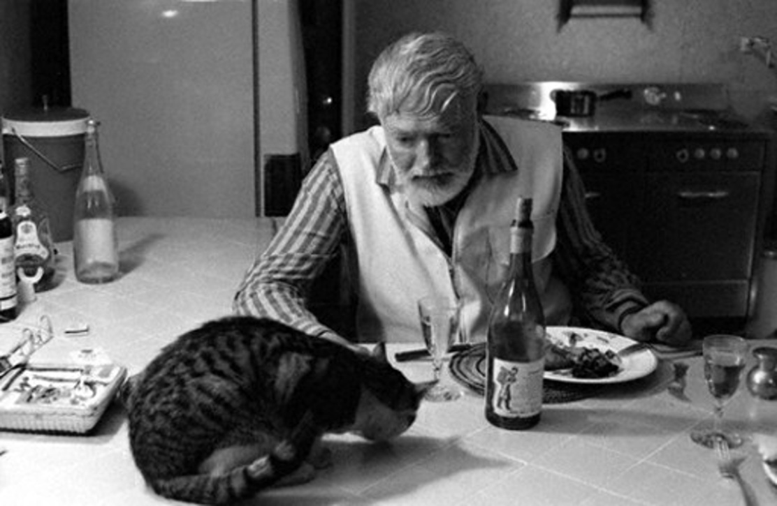 Эрнест Хемингуэй за ужином с котом - Большим Мальчиком Петтерсоном, 1959 год.jpg